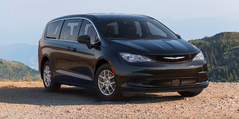 Black minivan parked on a gravel overlook with mountains and a clear sky in the background