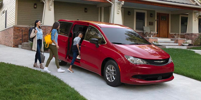 Red minivan parked in a residential driveway while people enter through the open sliding side door