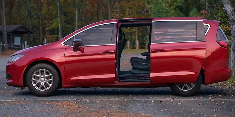 Side view of a red minivan parked outdoors with the sliding side door open, revealing the interior seating area