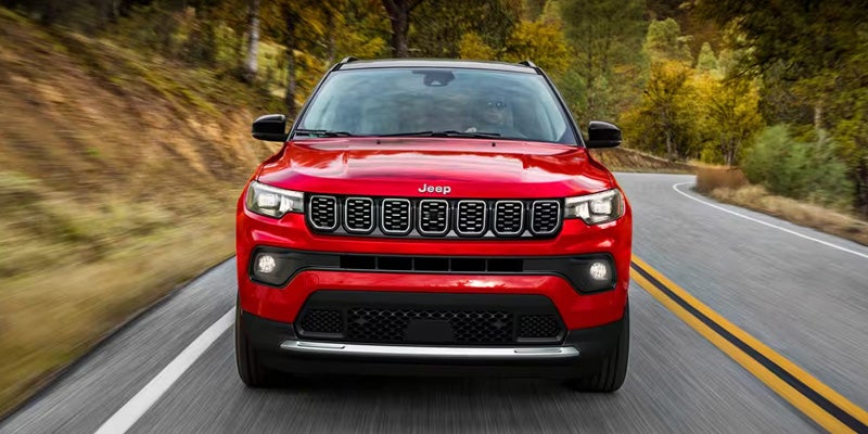 Red Jeep Compass SUV driving on a winding two-lane road surrounded by trees and natural scenery