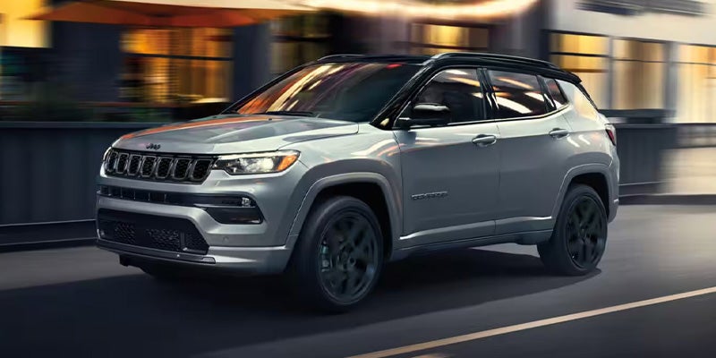 Silver Jeep Compass SUV driving through an urban street with blurred buildings in the background