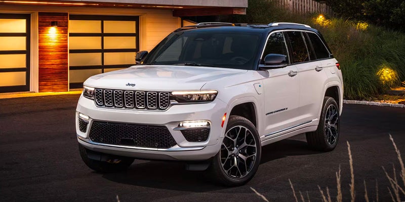 White Jeep Grand Cherokee 4xe SUV with a black roof, parked in a driveway in front of a modern garage at dusk