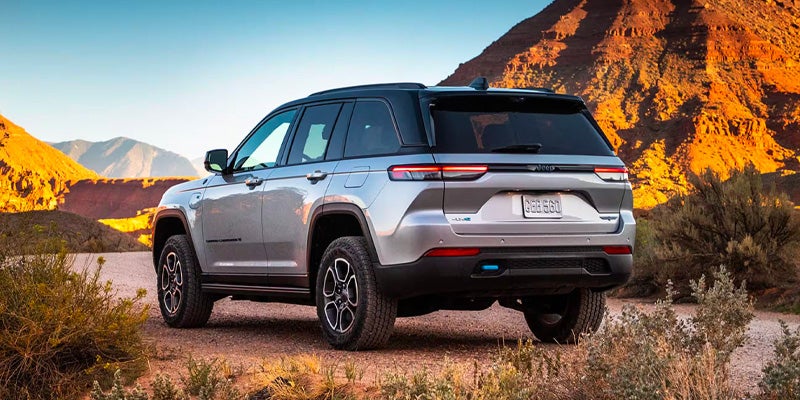 Silver Jeep SUV parked on a dirt trail surrounded by rocky desert mountains and sparse vegetation