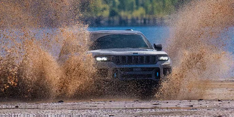 Dark gray SUV driving through muddy water, splashing mud high into the air with a lake in the background