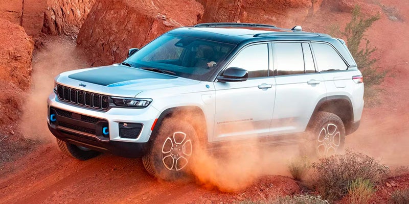 White Jeep Grand Cherokee 4xe off-roading, kicking up dust on reddish-orange rocky terrain