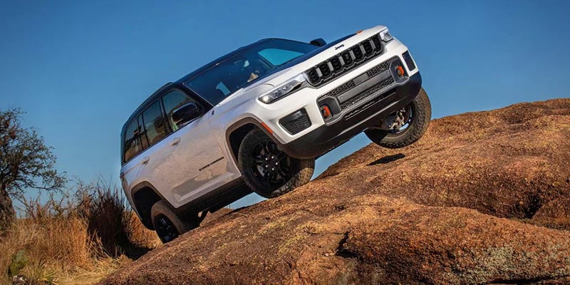 White Jeep SUV climbing a steep rocky hill on an off-road trail under a clear blue sky
