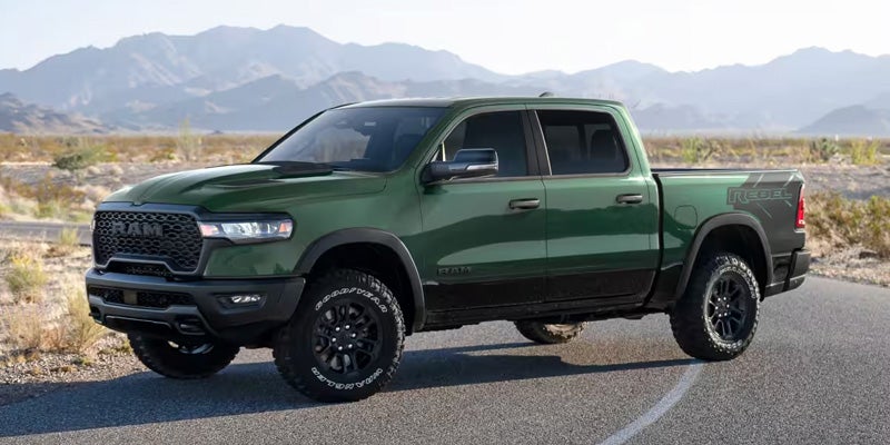 Green Ram pickup truck parked on a paved road in a desert landscape with mountains in the background.