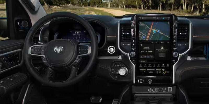 Ram truck interior featuring a steering wheel, digital instrument cluster, and a large vertical touchscreen displaying navigation