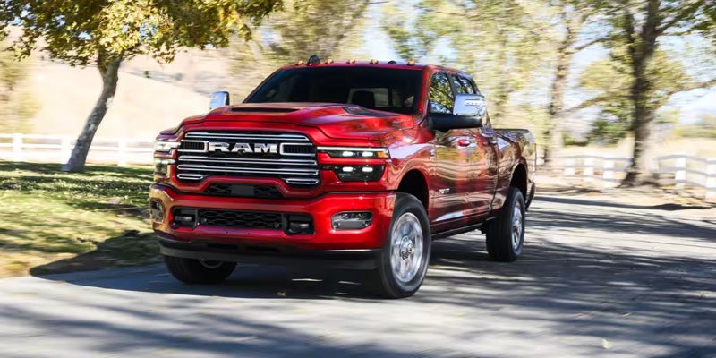 Red Ram pickup truck driving on a tree-lined road in a rural setting, viewed from the front at an angle