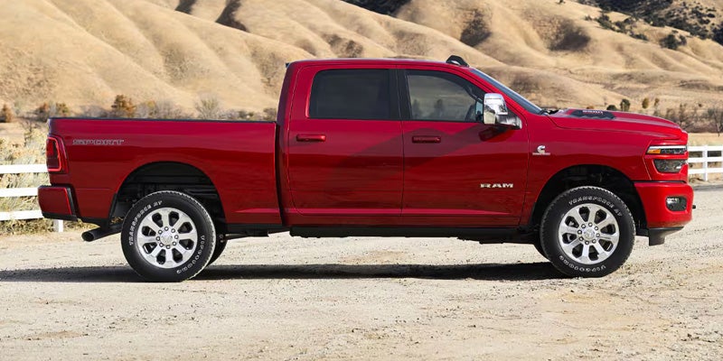 Side view of a red Ram pickup truck parked on a dirt surface with rolling hills in the background