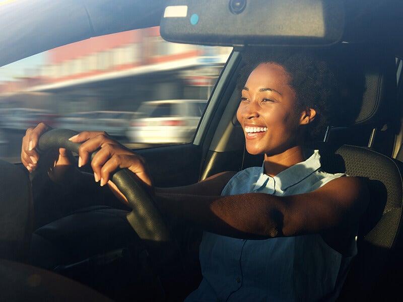 Smiling Black woman driving a car, hands on the wheel, with motion blur and sunlight