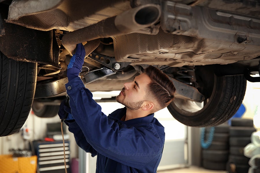 Mechanic in blue uniform and gloves works on the exhaust system of a car lifted on a hoist