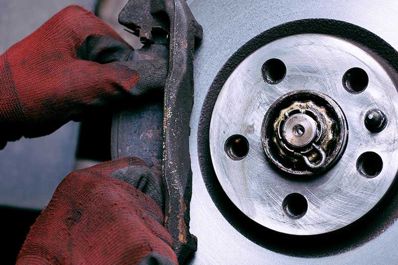 Close-up of an automotive brake rotor and brake pad, with gloved hands inspecting or replacing brake components during vehicle maintenance