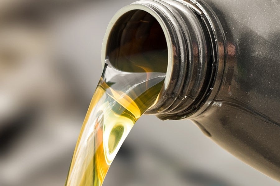 Close-up of golden motor oil being poured from a plastic container, showing a steady stream of engine oil flowing from the bottle opening