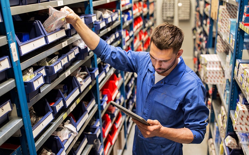 Automotive parts worker using a tablet to manage inventory while selecting a packaged component