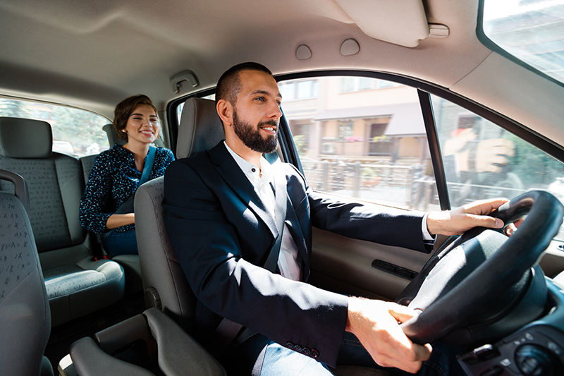 Man driving a car with a smiling woman passenger in the back seat